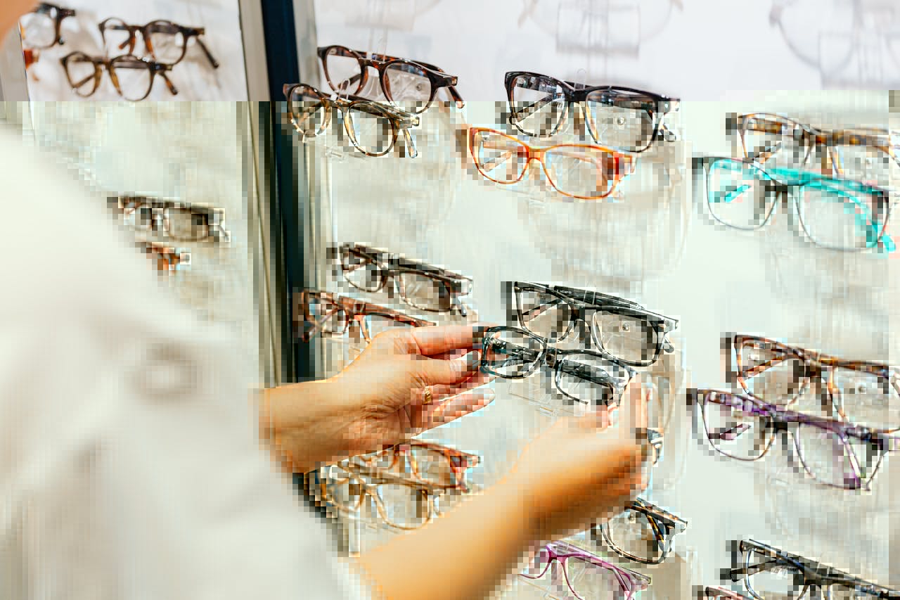 Hands selecting glasses from a display wall in an eyewear store.